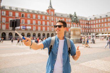 Mutlu ve heyecanlı eğleniyor çekici erkek İspanyol turist Plaza Mayor, Madrid, İspanya'selfie ile smartphone alarak. Seyahat, tatil, tatil Avrupa şehri kavram.
