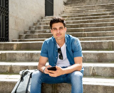 Kot denim giysileri Street modern Avrupa şehri ve modern smartphone cep telefonu ile mesaj merdivenlerde oturan genç mutlu erkek öğrenci