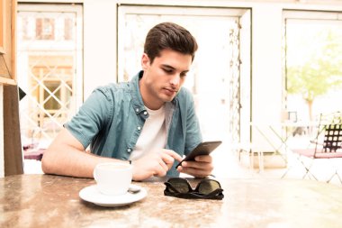 Yakışıklı adam kahve dükkanında mola sırasında kısa mesaj okuma doğal gıda kafede otururken cep telefonunda sohbet genç erkek serbest meslek