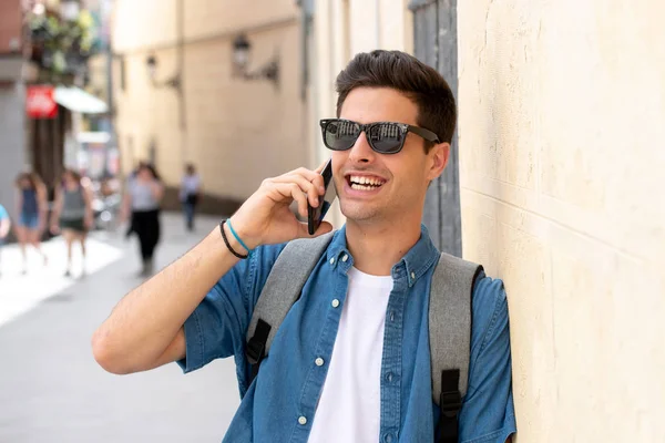ヨーロッパの都市で屋外で立って 携帯電話で話している 幸せと興奮を見て魅力的な若い男 都市の背景 通信技術の概念 — ストック写真