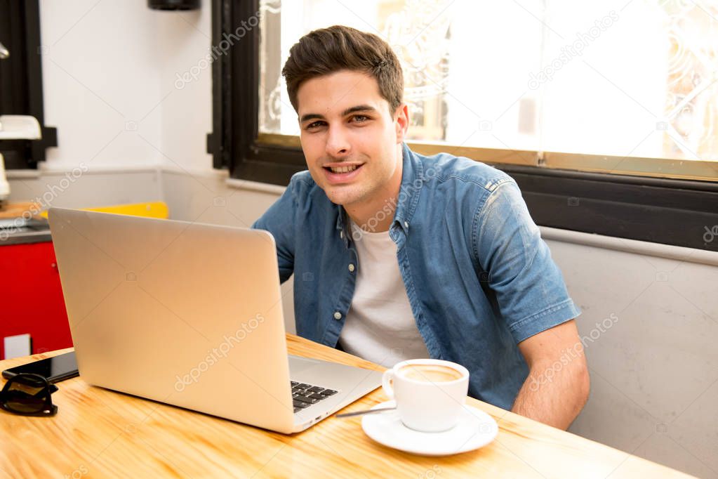 Portrait of young Hispanic man using laptop at cafe. Causally dressed student working on computer while drinking coffee in education communication concept