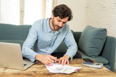 Laptop ile evde çalışan genç sinirli ve endişeli erkeğin faturaları seyir ve ev finansman kavramında fatura ödeme