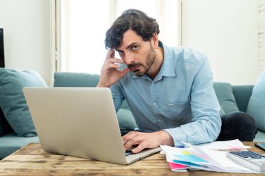 Laptop ile evde çalışan genç sinirli ve endişeli erkeğin faturaları seyir ve ev finansman kavramında fatura ödeme