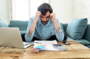 Laptop ile evde çalışan genç sinirli ve endişeli erkeğin faturaları seyir ve ev finansman kavramında fatura ödeme