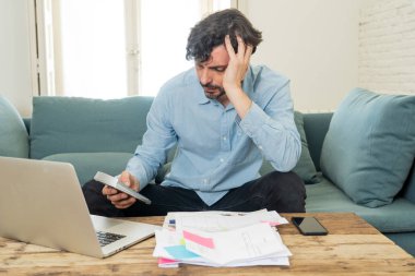 Laptop ile evde çalışan genç sinirli ve endişeli erkeğin faturaları seyir ve ev finansman kavramında fatura ödeme