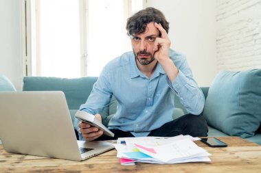 Laptop ile evde çalışan genç sinirli ve endişeli erkeğin faturaları seyir ve ev finansman kavramında fatura ödeme