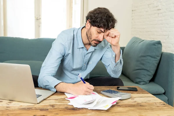 young angry and worried man working with laptop at home looking at bills and paying bills in home finance concept