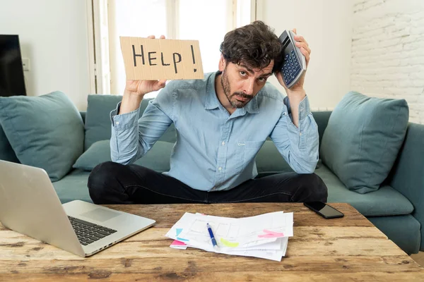 young angry and worried man working with laptop at home holding a help sign looking at bills and paying bills in home finance concept