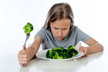 Beslenme ve sağlıklı beslenme alışkanlıkları çocuklar sağlıklı beslenme kavramı için. Çocuk sebze yemeyi sevmiyorum. Küçük sevimli kız beyaz bir arka plan üzerinde sağlıklı brokoli yemek reddediyorum