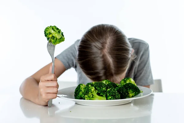 Nutrition and  healthy eating habits for kids healthy eating concept. Children do not like to eat vegetables. Little cute kid girl refuse to eat healthy broccoli  on a white background