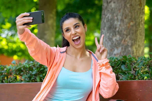 スリムな大人セクシーなフィットを探して良い近代的な都市公園は 運動をして翌朝のスポーツ ウエアでスポーティなラテン女性は Selfie 彼女の電話でフィットネスと — ストック写真
