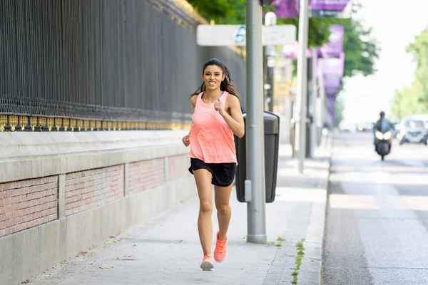 attractive young latin female runner jogging on the city street with traffic on the road in a  city environment