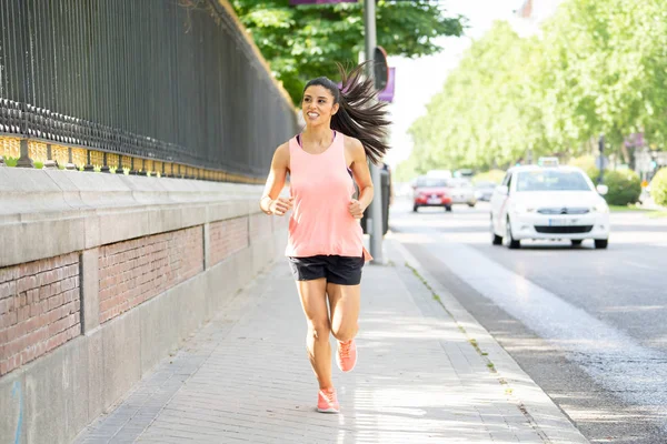 attractive young latin female runner jogging on the city street with traffic on the road in a  city environment
