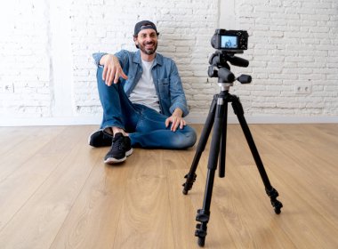 Hippi tarzı video kamera tripod karşı tuğla duvar arka planda internet blog ve blogger kavramı üzerinde rahat kıyafetler genç çekici adam.