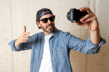 Hippi tarzı modern bir görünüm kendi kendine portre çekim ya da yazmak video internet blog ve blogger kavramında fotoğraf kamera tutarak rahat kıyafetler giymiş genç çekici adam.