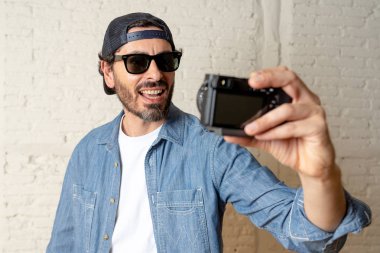 Hippi tarzı modern bir görünüm kendi kendine portre çekim ya da yazmak video internet blog ve blogger kavramında fotoğraf kamera tutarak rahat kıyafetler giymiş genç çekici adam.