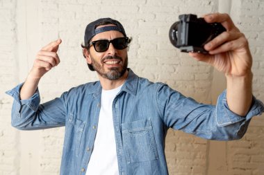 Hippi tarzı modern bir görünüm kendi kendine portre çekim ya da yazmak video internet blog ve blogger kavramında fotoğraf kamera tutarak rahat kıyafetler giymiş genç çekici adam.