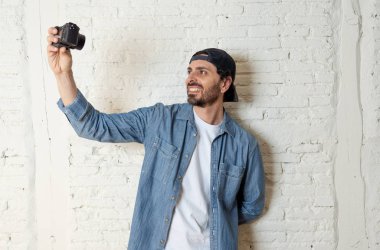 Hippi tarzı modern bir görünüm kendi kendine portre çekim ya da yazmak video internet blog ve blogger kavramında fotoğraf kamera tutarak rahat kıyafetler giymiş genç çekici adam.