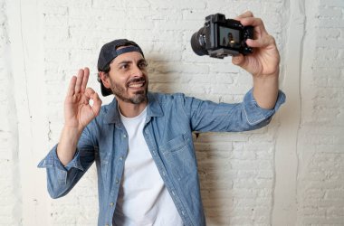 genç çekici adam hippi tarzı modern bir görünüm kendi kendine portre çekim ya da yazmak video internet blog ve blogger kavramında fotoğraf kamera tutarak rahat kıyafetler giyiyor. Tamam gösterilen adam