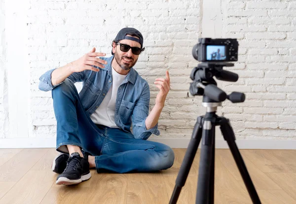 Hippi tarzı video kamera tripod karşı tuğla duvar arka planda internet blog ve blogger kavramı üzerinde rahat kıyafetler genç çekici adam.