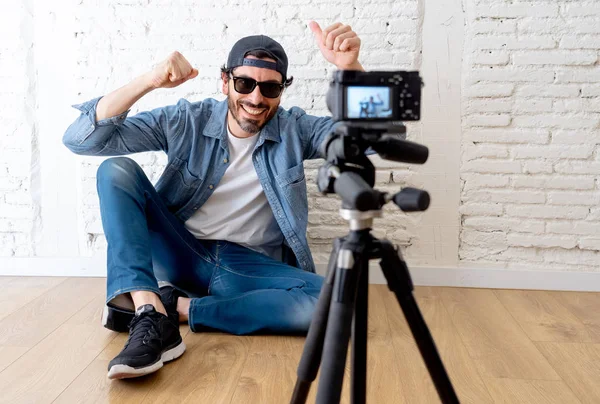 çekici genç hippi tarzı video kamera tripod karşı tuğla duvar arka planda internet blog ve blogger kavramı üzerinde rahat kıyafetler içinde. başparmak göstermek yukarıya adam