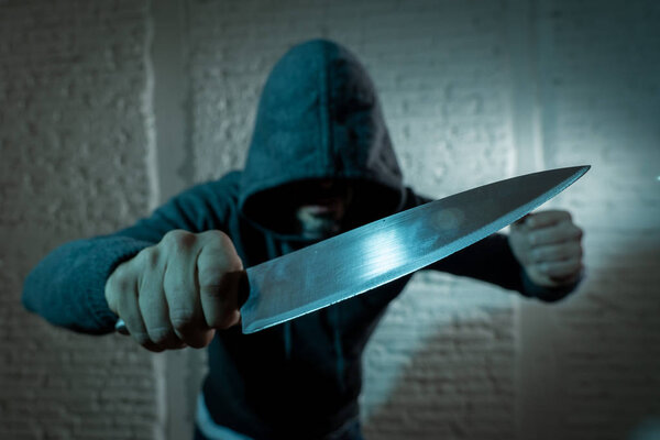 close up of hand holding a knife of dangerous hooded man standing in the dark.  London knife crime concept.