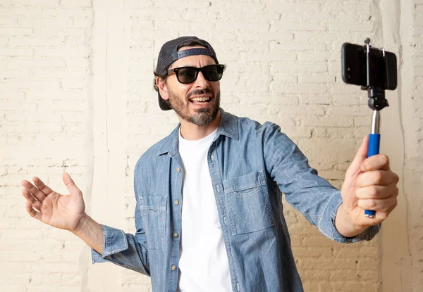若い魅力的な男性カジュアルな服を着て セルフ ポートレート写真を撮影またはビデオ録画 Selfie スティック携帯電話を保持している流行に敏感なスタイルの帽子 インターネットのブログやブロガーのコンセプト — ストック写真