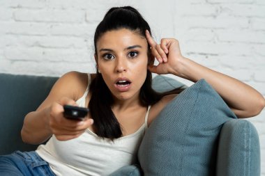 genç güzel latin kadın evde koltuk kanepe oturma odasında televizyon korkunç korku filmi ya da korkmuş ve Uzaktan kumanda tutan gözlerini kapsayan heyecanlı korkunç haber izlerken oturuyordu.