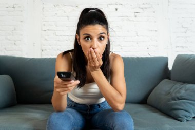 genç güzel latin kadın evde koltuk kanepe oturma odasında televizyon korkunç korku filmi ya da korkmuş ve Uzaktan kumanda tutan gözlerini kapsayan heyecanlı korkunç haber izlerken oturuyordu.