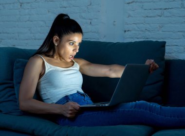 rahat kıyafetler kanepe çalışma üzerinde oturan güzel İspanyol internet bağımlısı genç kadında bıkkın ve yorgun dizüstü bilgisayar ile gece ışık karanlık odada geç işten yorgun.