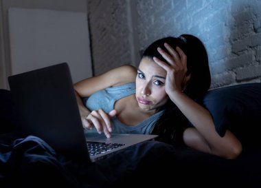 genç güzel İspanyol internet bağımlısı kadın yatakta bıkkın ve yorgun dizüstü bilgisayar ile karanlık bir odada hafif esneme yorgun düşen uyku gece geç saatlerde çalışan ev yatak odası, pijama.