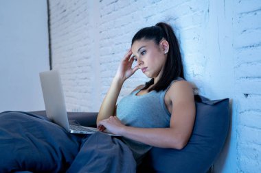 genç güzel İspanyol internet bağımlısı kadın yatakta bıkkın ve yorgun dizüstü bilgisayar ile karanlık bir odada hafif esneme yorgun düşen uyku gece geç saatlerde çalışan ev yatak odası, pijama.