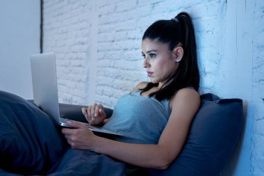 genç güzel İspanyol internet bağımlısı kadın yatakta bıkkın ve yorgun dizüstü bilgisayar ile karanlık bir odada hafif esneme yorgun düşen uyku gece geç saatlerde çalışan ev yatak odası, pijama.