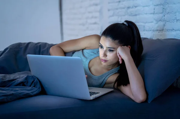美しいラテン語インターネット中毒女性作業と中毒デバイス概念で驚いて見て暗い部屋で夜遅く退屈 眠れない 疲れて自宅に彼女のベッドで彼女のコンピューター上でサーフィン — ストック写真