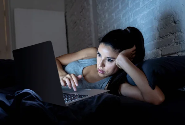 美丽的拉丁互联网上瘾的妇女工作和冲浪在她的电脑无聊 失眠和疲惫 在她的床上深夜在黑暗的房间里看着惊讶成瘾装置概念 — 图库照片