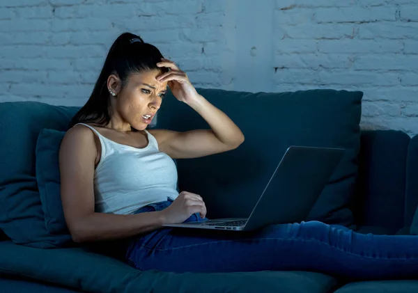 ジーンズと深夜技術中毒の概念でチャット ソーシャル ネットワークを使用してラップトップ コンピューターを持つソファ驚き顔の表現に一重項で若い美しいヒスパニック女性インターネット中毒 — ストック写真