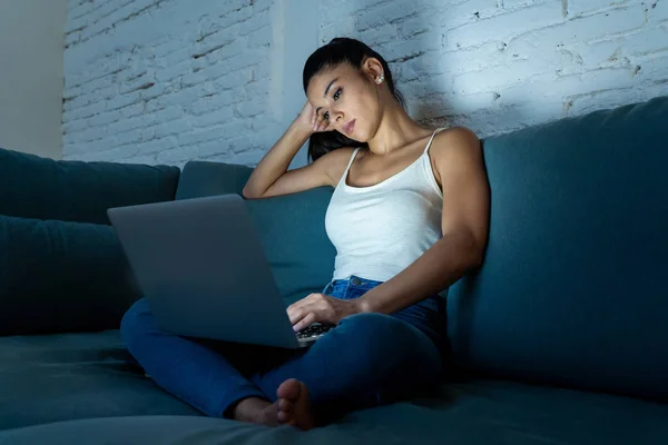 ソファ作業の上に座って私服で若いの美しいヒスパニック系インターネットの常習者の女性を退屈し 仕事からパソコンに疲れて暗い部屋の光で夜遅く疲れ — ストック写真