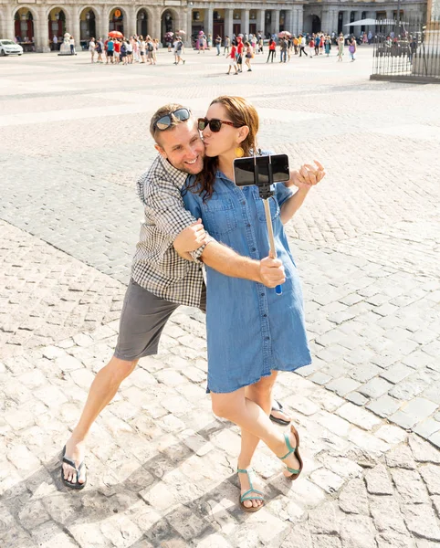 Happy couple taking pictures with selfie stick on Plaza Major in the old town of Madrid, Spain. Tourists people taking travel photos with smart phone on summer holidays.