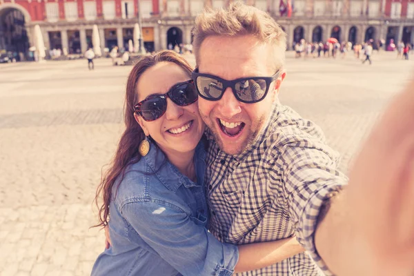 Happy couple taking selfie on Plaza Major in the old town of Madrid, Spain. Tourists people taking travel photos with smart phone on summer holidays.