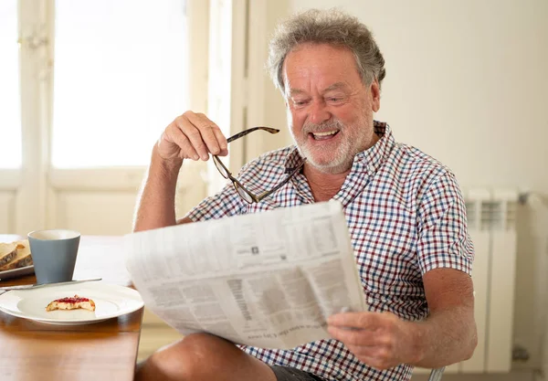 Portrait of happy senior old man with grey hair reading the newspaper while having breakfast and drinking coffee. Happy old age retirement concept.