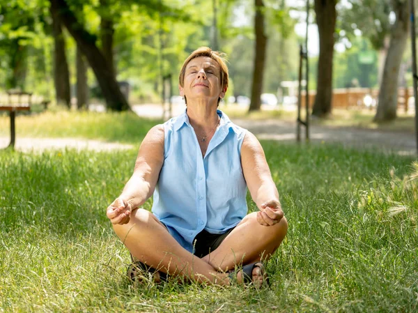 Senior woman in a meditative yoga pose sitting on green grass.