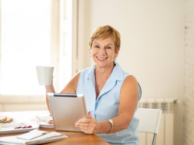 Gülümseyen kadın kıdemli dijital tablet kahvaltı ve kahve evde içme kullanma. 