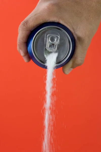 Hand holding a soda can pouring sugar