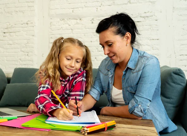 Beautiful mother helping her young blonde cute sweet girl doing homework at home. Homework parenting and education concept