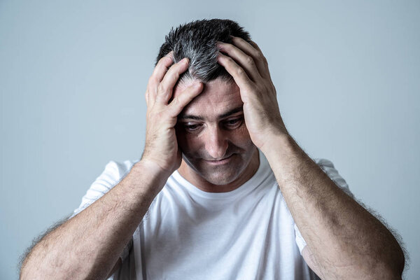 Portrait of an attractive man sad an depressed suffering depression feeling sorrow and pain in human emotions facial expressions and depression concept isolated on grey blue background