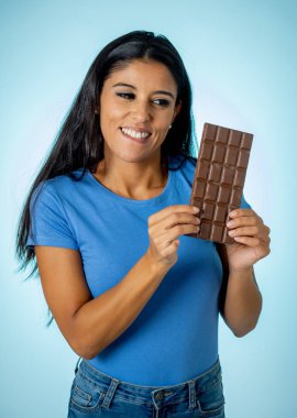 Güzel genç Şirin ve mutlu latin kadını rahat kıyafetler büyük lezzetli çikolata tablet diyet görmezden ve tatlı abur cubur yeme arka plan izole Eğer düşünme günaha ile seyir holding