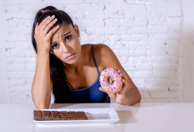 Hungry beautiful young woman unhappy craving sweet chocolate and doughnuts and cannot eat in Dieting Weight loss Sugar addiction Diabetic and unhealthy healthy food concept. clipart