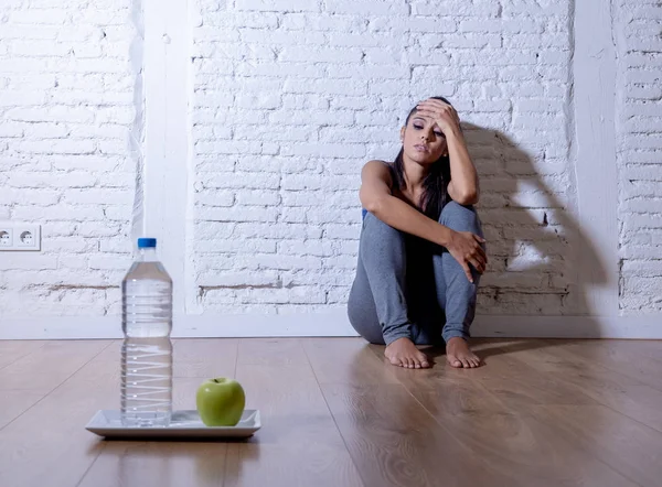 绝望的节食年轻妇女坐在地上看着悲伤的一个苹果水果和水作为疯狂饮食意志力和营养紊乱的象征 — 图库照片