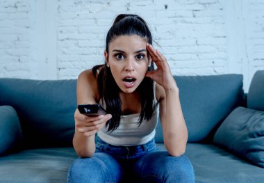 Güzel latin kadın korkmuş korkmuş ve yalnız evde oturma odasında kanepede oturup televizyon bir korku filmi izlerken tiksinti.