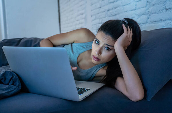 Tired attractive young woman working and surfing on the internet with computer on the sofa at home late at night in internet addiction and overwork concept.